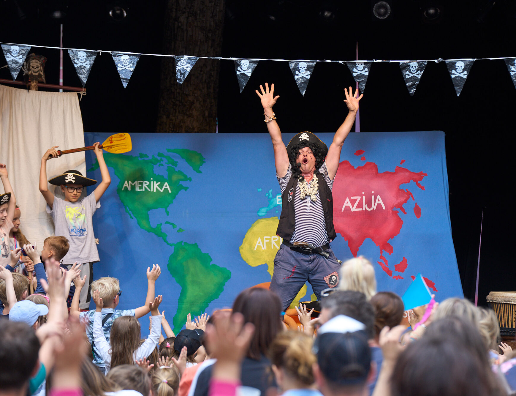 A pirate is preforming on stage in festival Lent, in Maribor. Children are sitting and raising hands as a participation of preformance.