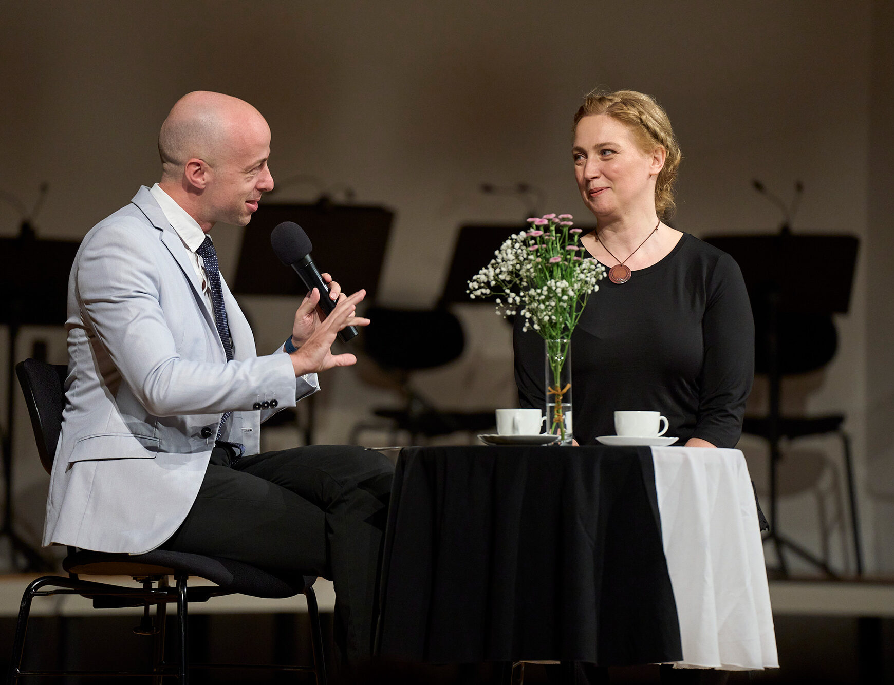 The play is taking place in Unionska dvorana and the actors are sitting by the table. A man is talking and a woman is listening.